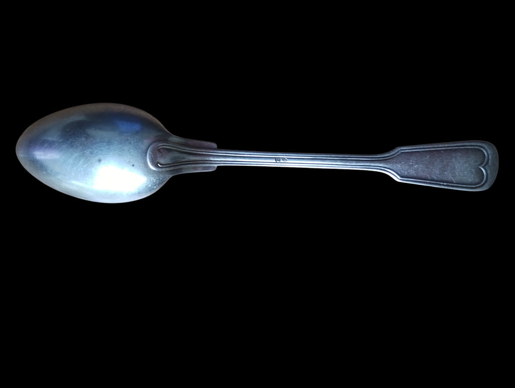 Back view of a vintage spoon showing the handle pattern, small stamp, and surface wear
