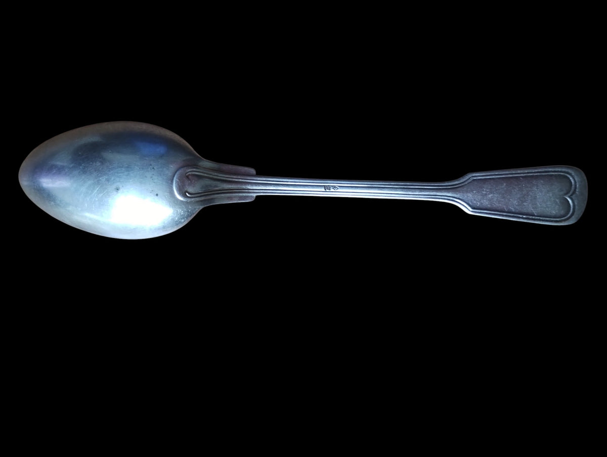 Back view of a vintage spoon showing the handle pattern, small stamp, and surface wear
