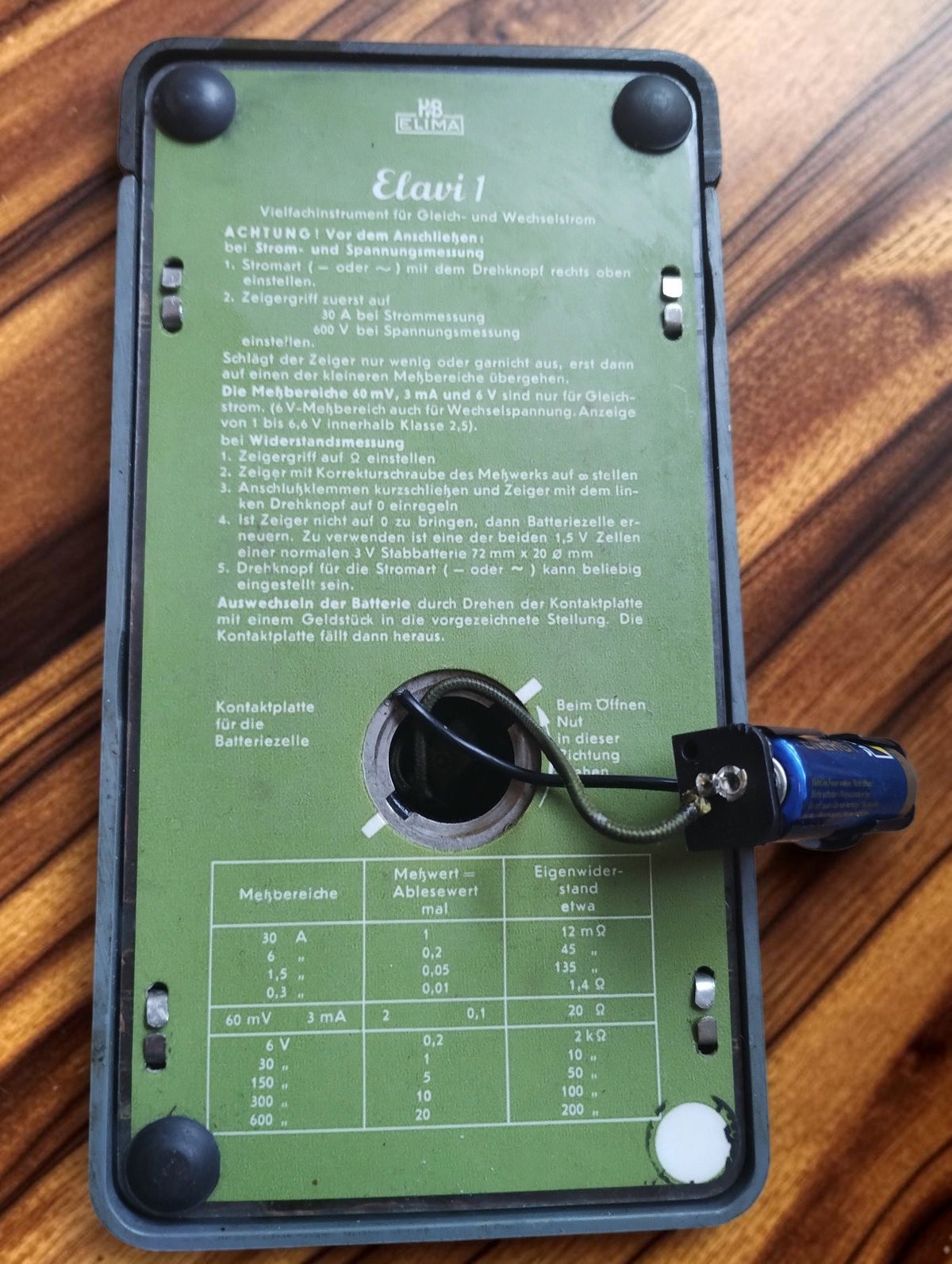 Underside of the ELIMA Elavi 1 multimeter with green German instruction panel and connected battery holder
