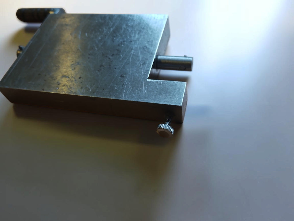 Angled close-up of a metal hinge filing jig showing the recessed corner, shaft and knurled screw.