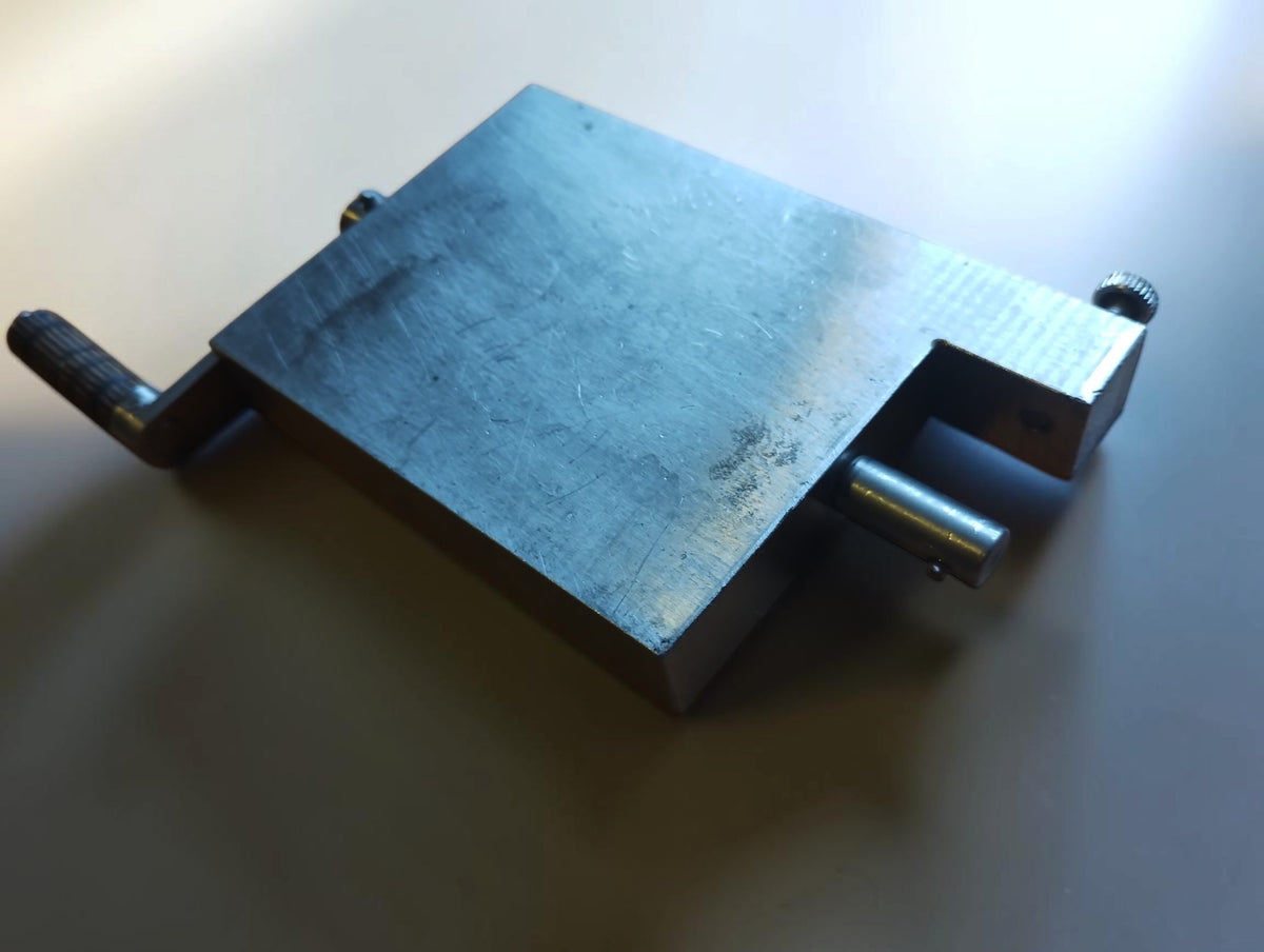 Metal hinge filing jig viewed diagonally from above, showing the crank, recessed corner and surface wear.