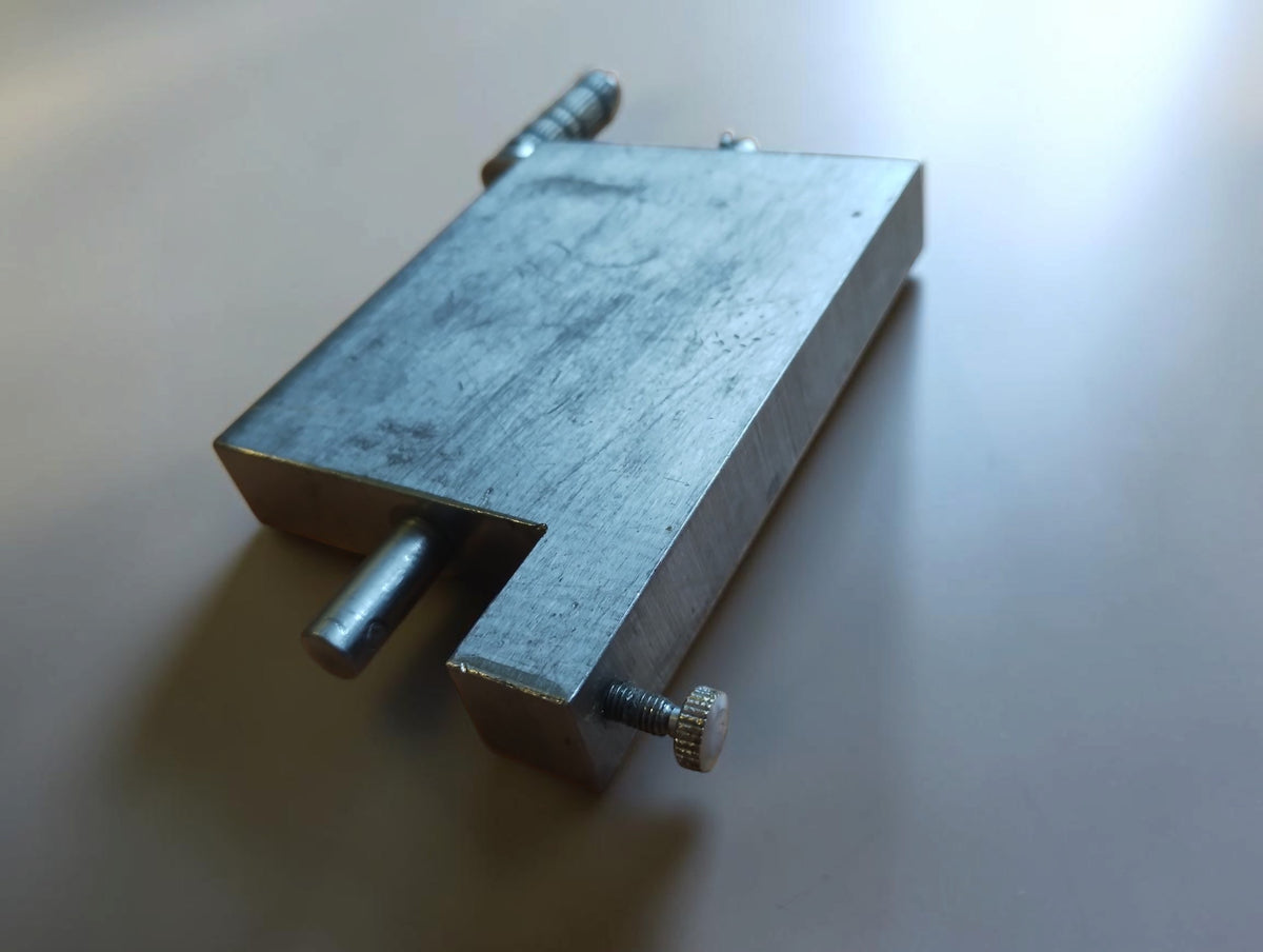 End view of a metal hinge filing jig showing the cylindrical shaft, side screw and worn metal surface.