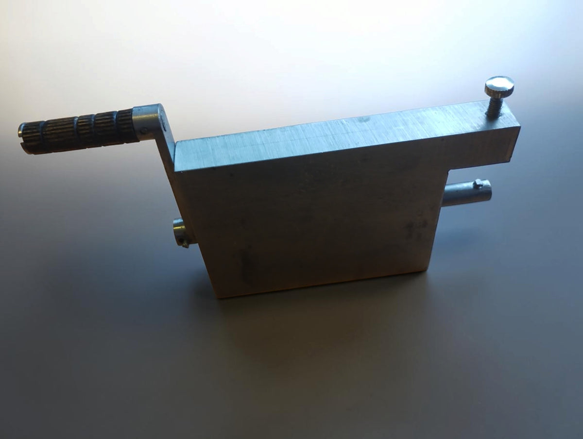 Metal hinge filing jig standing on its edge, showing the hand crank, screw and projecting shaft.
