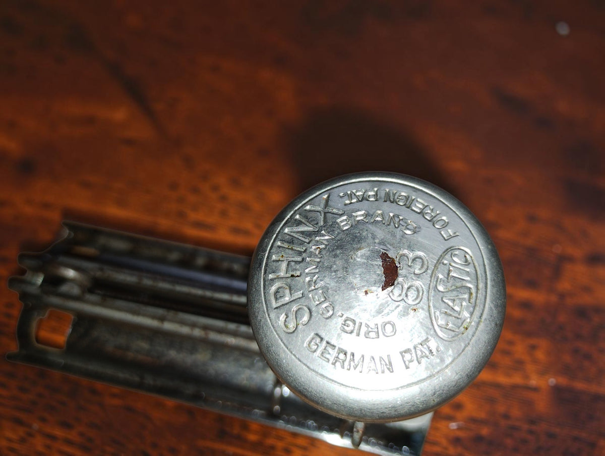 Detail van de ronde drukknop met Sphinx 83, Elastic en patentmarkeringen
