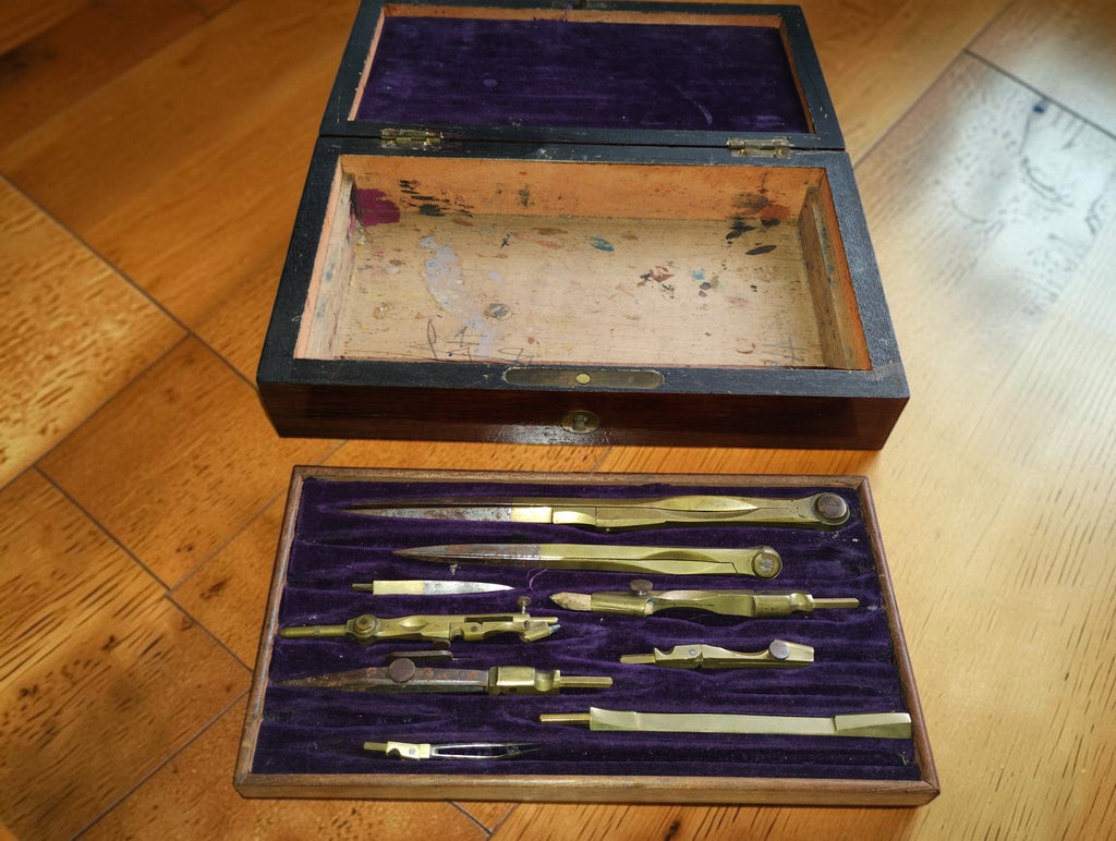 Uitneembare inleg met vintage tekeninstrumenten vóór de geopende houten kist met lege opbergruimte

