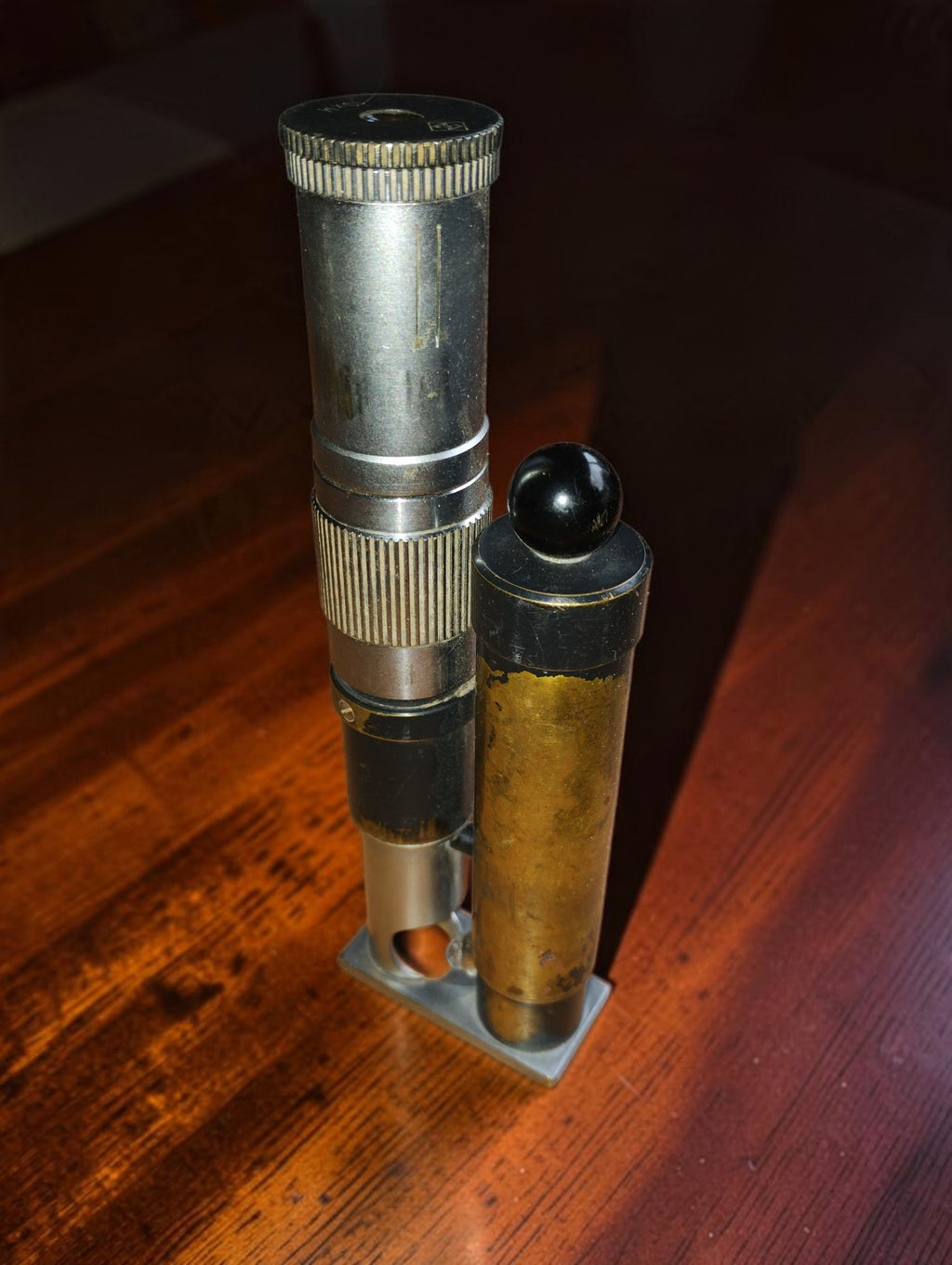 Vintage 10xM inspection microscope with attached lamp cylinder on a rectangular metal base, front view.

