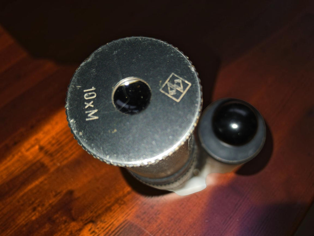 Close-up of the microscope eyepiece marked 10xM with a diamond-shaped maker’s mark.
