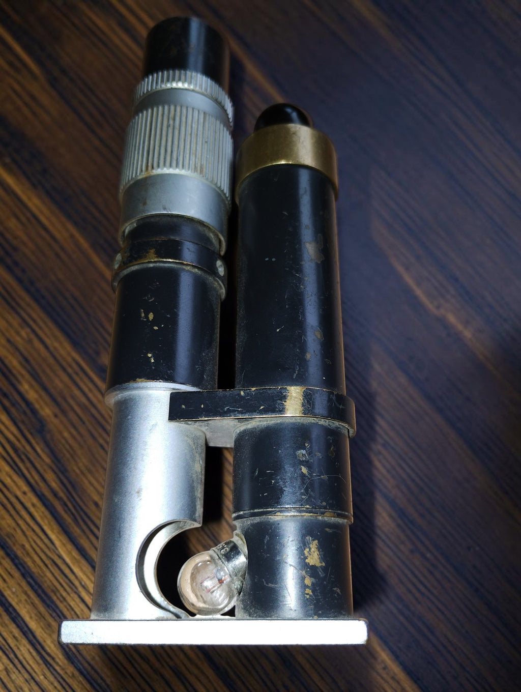Vintage inspection microscope showing the small light bulb beside the optical tube and wear to the black finish.
