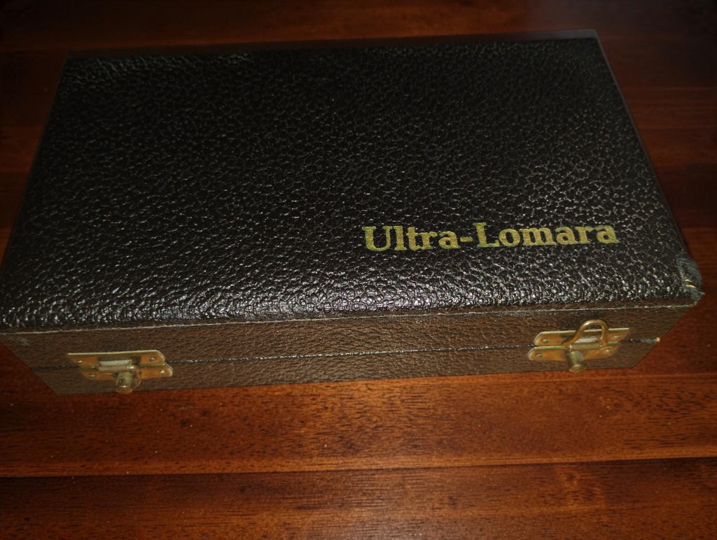 Closed black textured case with gold Ultra-Lomara lettering and two metal clasps.
