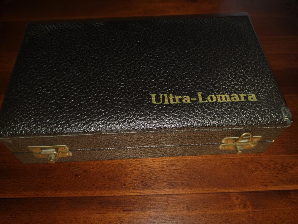 Closed black textured case with gold Ultra-Lomara lettering and two metal clasps.

