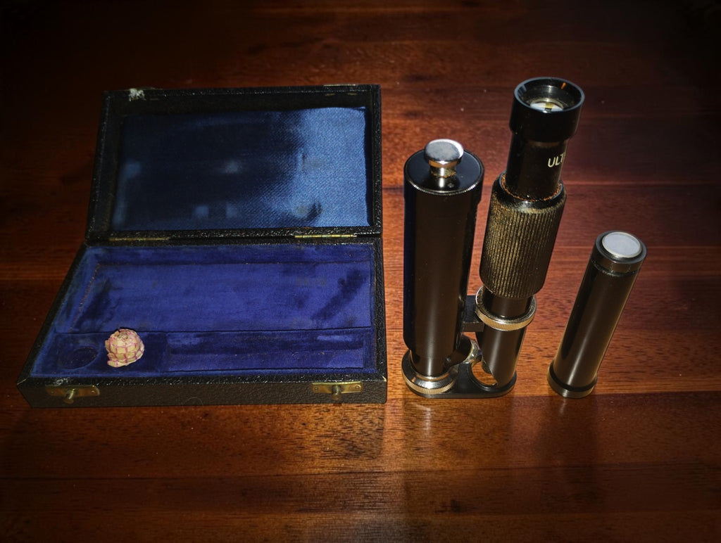 
Ultra-Lomara pocket microscope beside its open case, with a separate black tube on the right.

