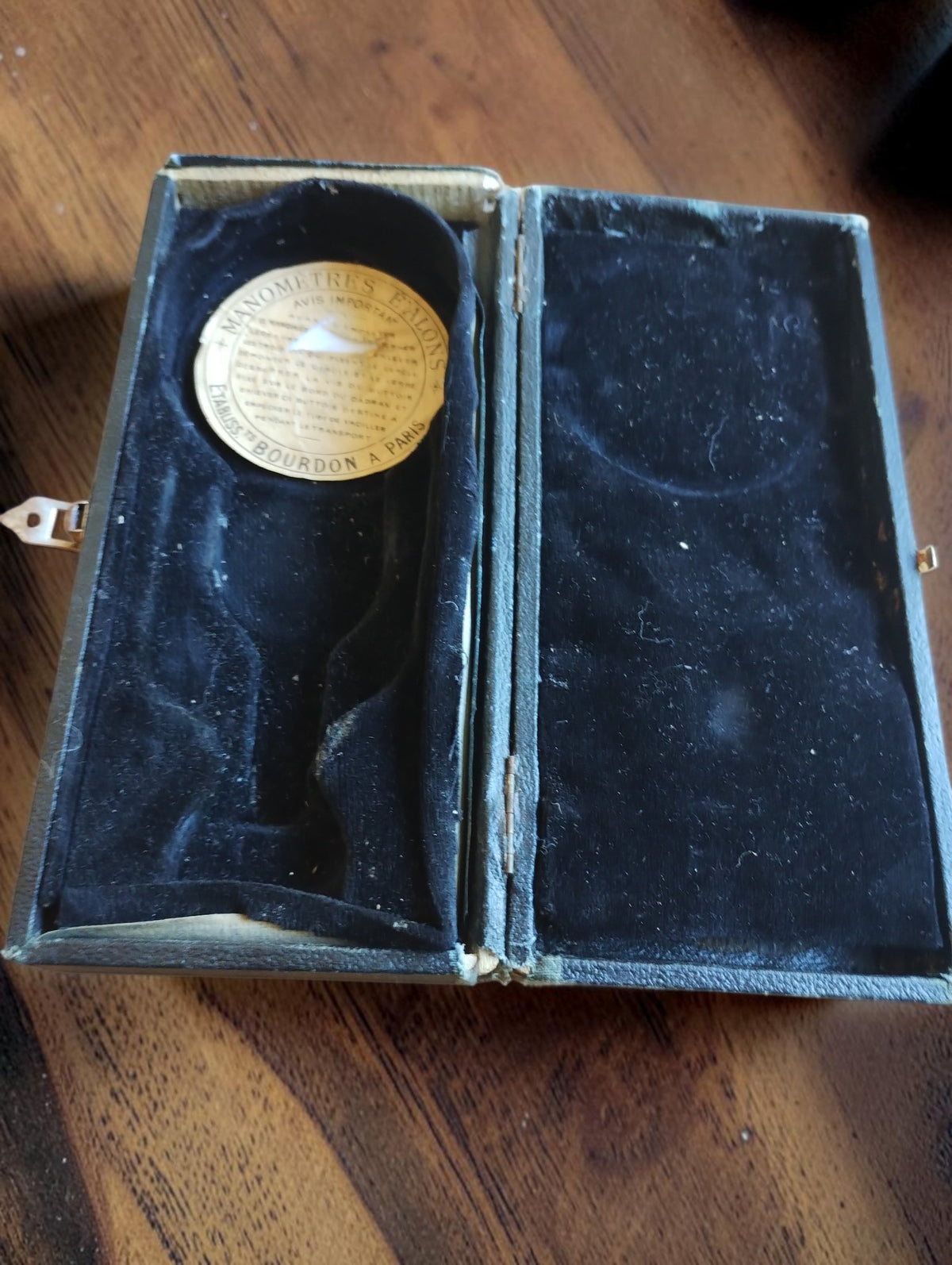 Interior of the vacuum gauge case with dark lining and a round maker’s label
