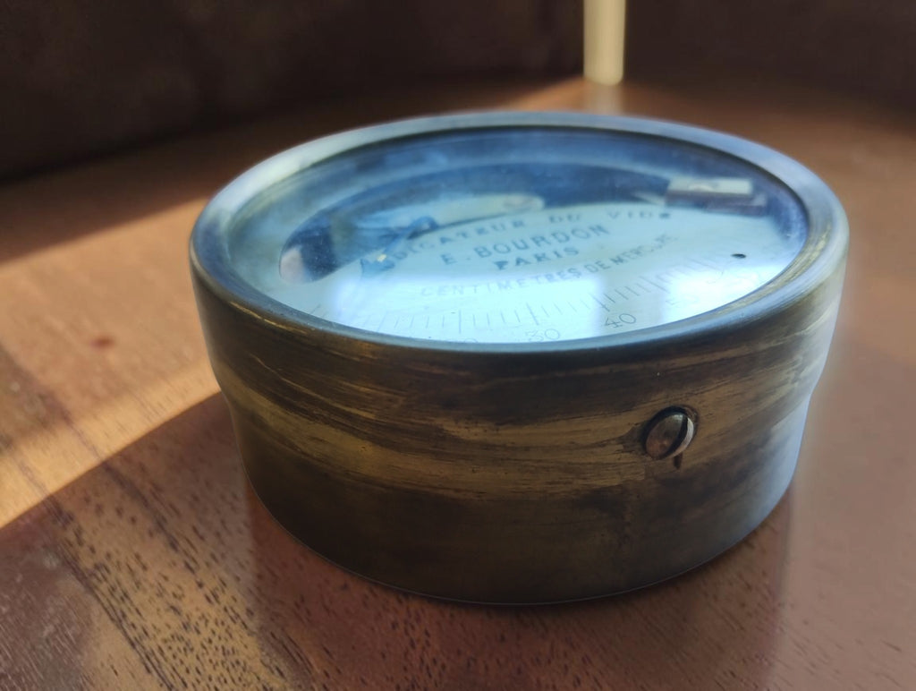 Side view of the E. Bourdon Paris vacuum gauge showing its metal housing and glass dial cover
