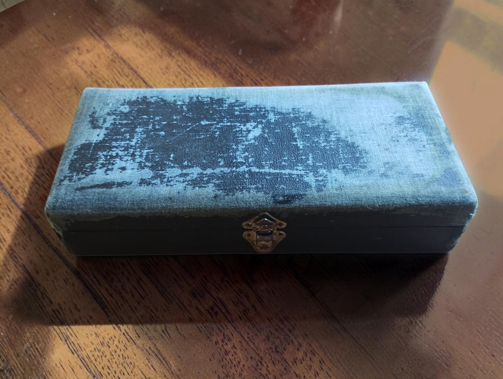Closed vacuum gauge storage case showing its clasp and worn outer covering
