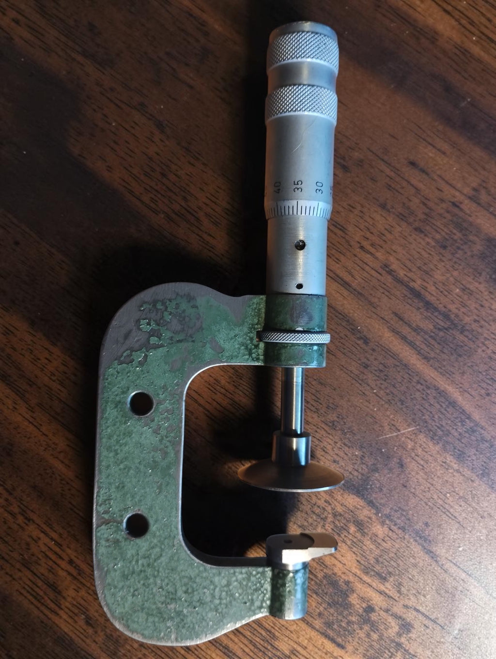 Vintage disc micrometer with a green frame and broad disc-shaped measuring faces on a wooden surface

