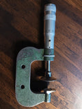 Vintage disc micrometer with a green frame and broad disc-shaped measuring faces on a wooden surface
