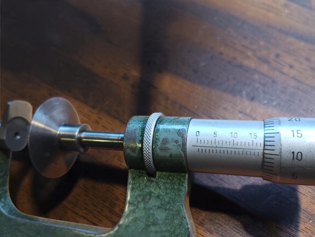 Close-up of the vintage disc micrometer showing the engraved scale, knurled collar and measuring faces
