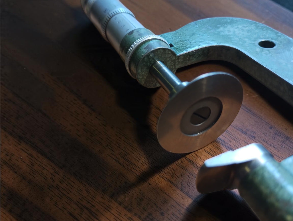 Angled close-up of the micrometer’s circular measuring disc, spindle and worn green frame
