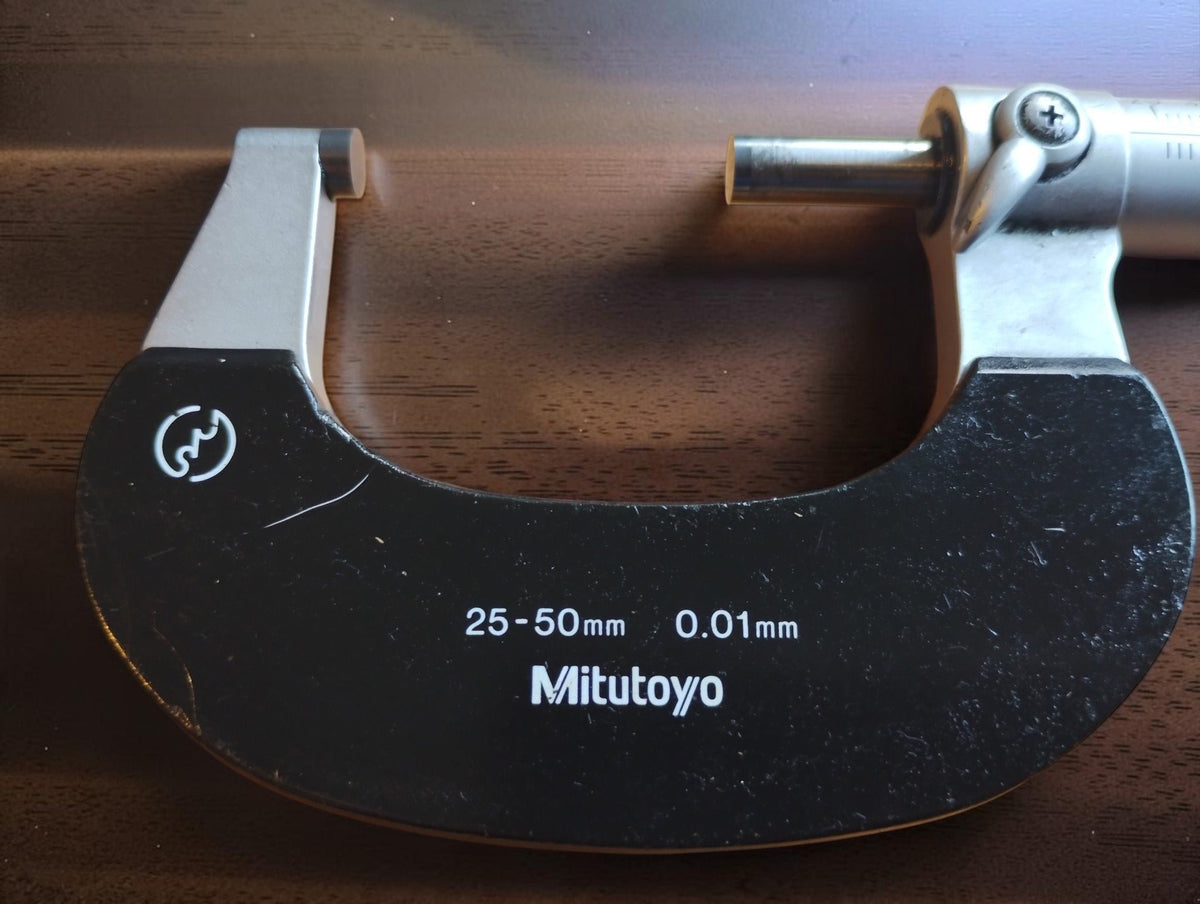 Black micrometer frame showing the Mitutoyo name, 25–50 mm range and 0.01 mm graduation marking.
