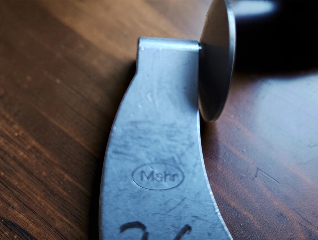 Close-up of the oval Mahr maker’s mark on the worn metal micrometer frame.
