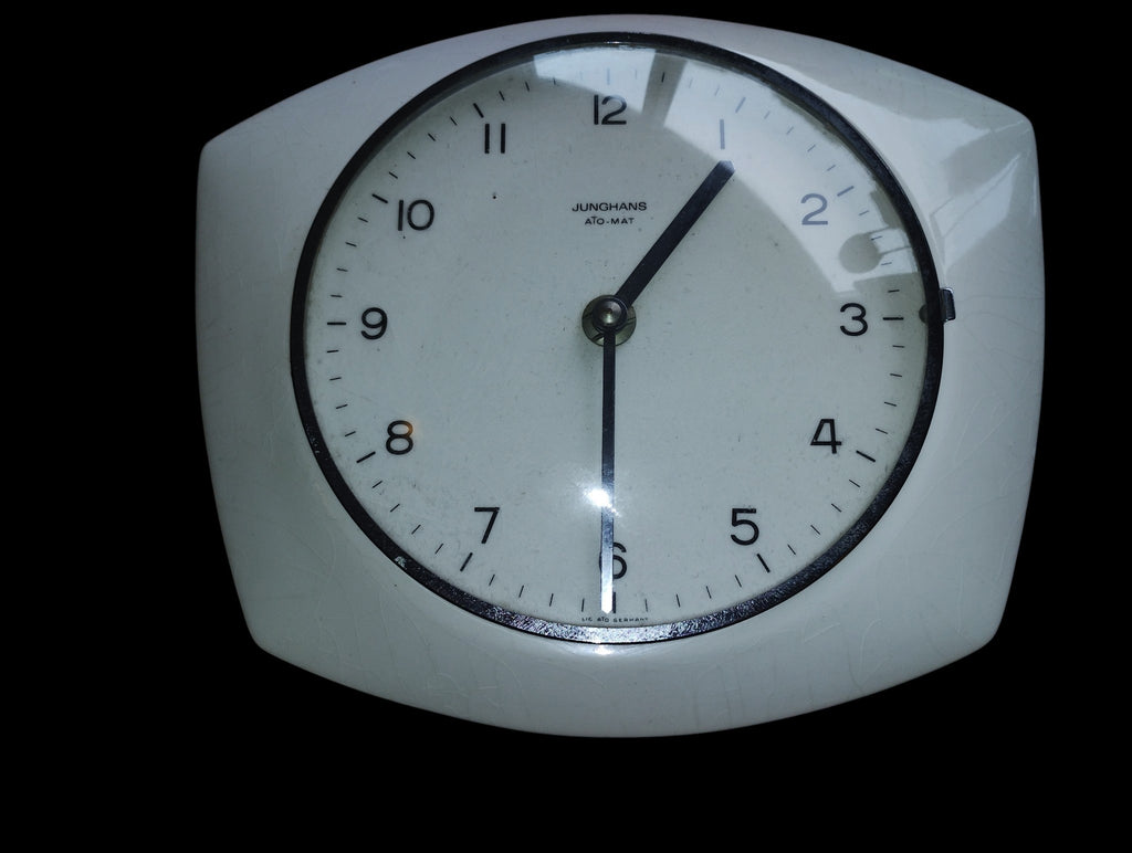 Front view of a white ceramic Junghans ATO-MAT wall clock with black numerals and hands.
