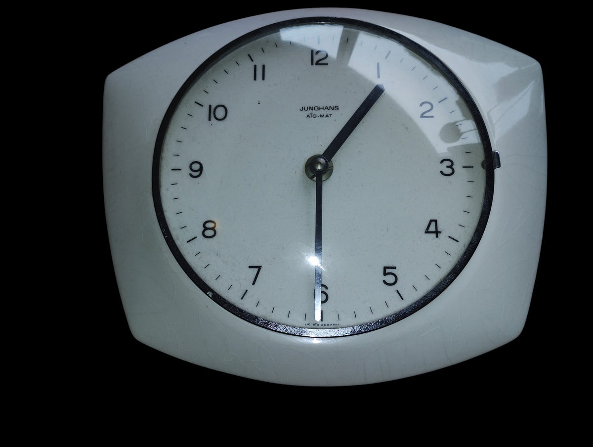 Front view of a white ceramic Junghans ATO-MAT wall clock with black numerals and hands.
